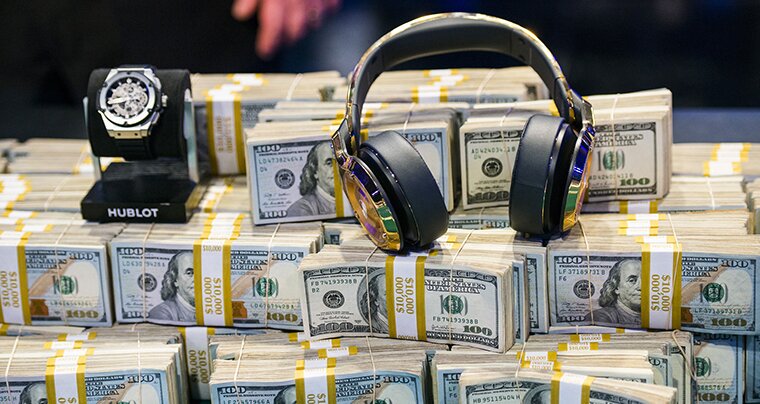 A large pile of stacks of hundred dollar bills with a luxury watch and pair of headphones on top.